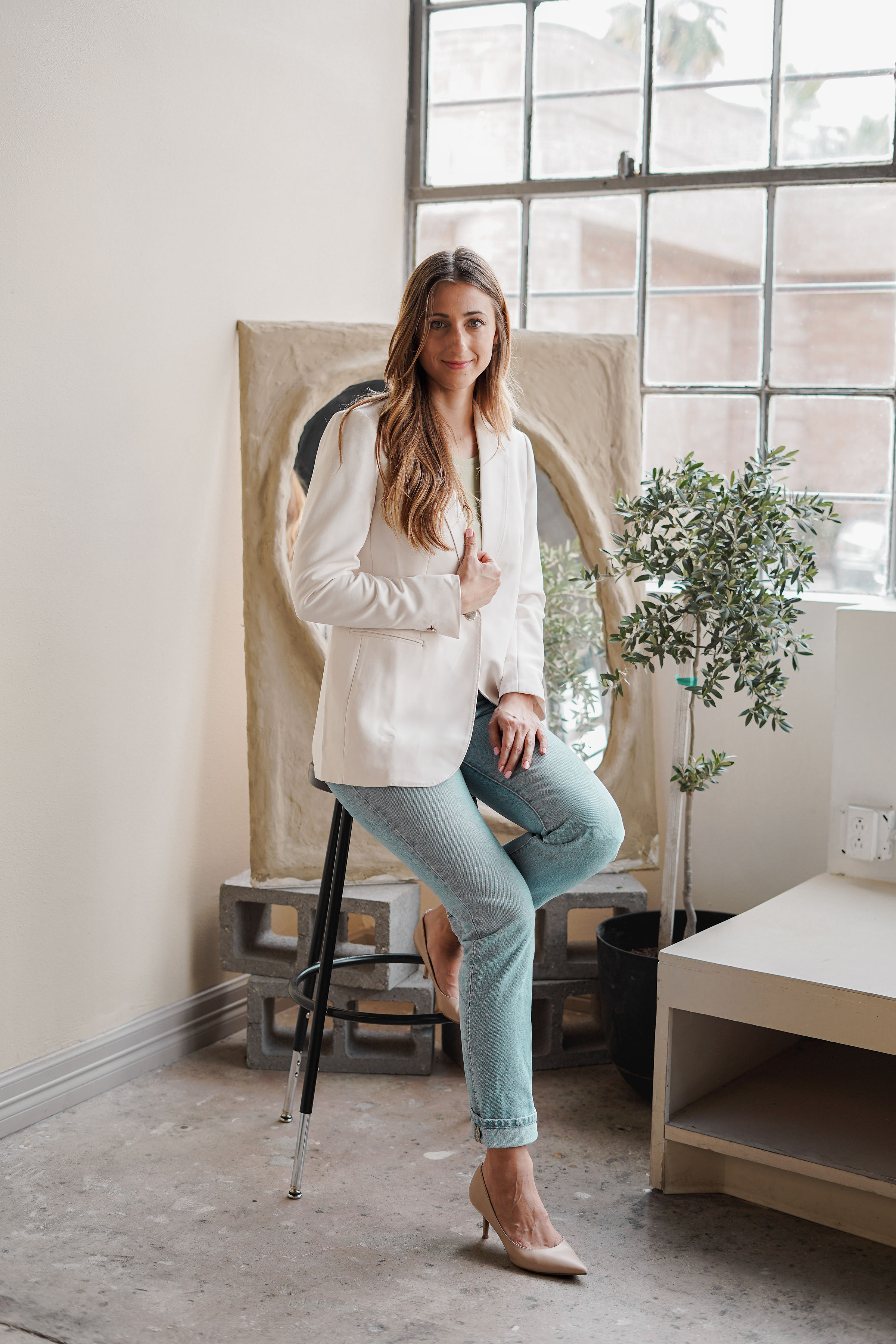 Krystina Holquin seated in a bright studio, wearing a white blazer